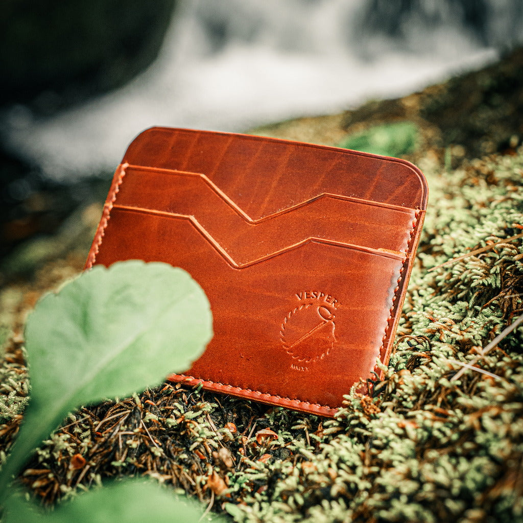 Brown leather wallet on mossy floor with waterfall in the background.