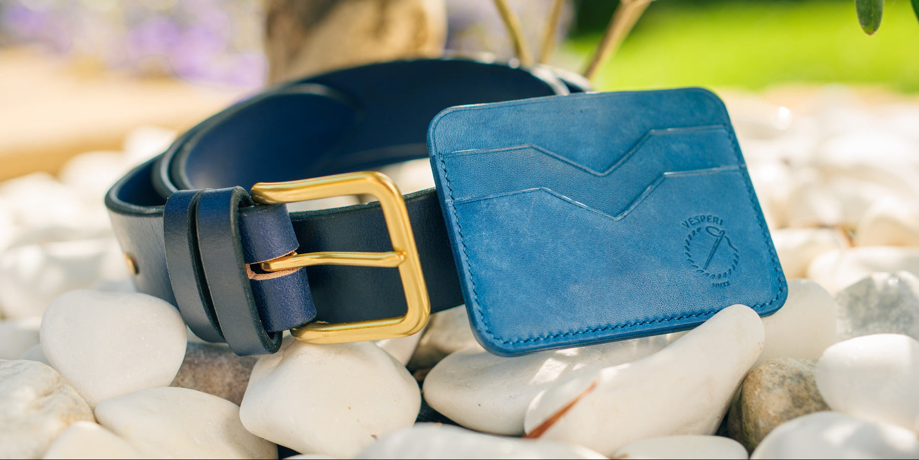 Blue leather belt and wallet on pebbles with a blurred natural background